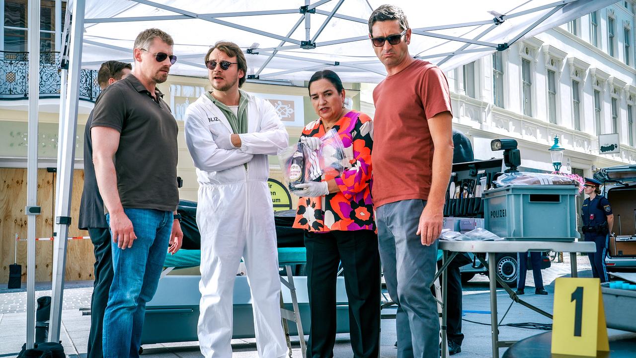 © ORF/Satel Film/Petro Domenigg Max, Julius, Franziska und Klaus stehen am abgesperrten Tatort unter einem Zelt mit einem Tisch, Ausrüstung und einem gelben Beweismarker.