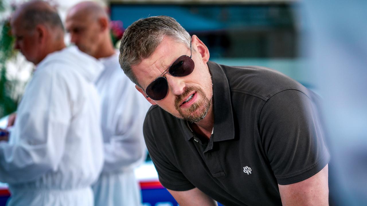 © ORF/Satel Film/Petro Domenigg Max Herzog beugt sich im Freien nach vorne, während im Hintergrund zwei Männer in weißen Schutzanzügen unscharf zu sehen sind.