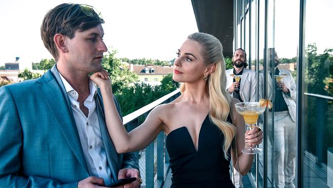 © ORF/Gebhardt Productions/Hubert Mican Silvia Schneider mit einem Cocktail in der Hand berührt das Kinn von Hubert Steiner auf der Terasse eines modernen Gebäudes