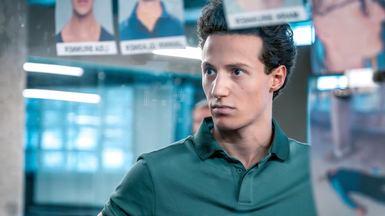 Damyan Andreev steht vor vor einer Wand mit Fotos und Namensschildern, im Hintergrund ein modern beleuchteter Raum.
