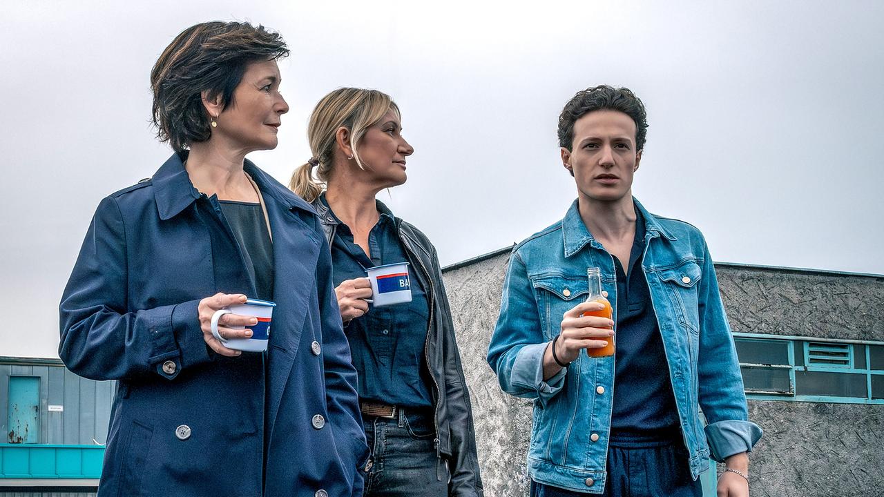Katharina Stemberger und Angelika Niedetzky mit Tasse in der Hand und Damyan Andreev mit einer Getränkeflasche stehen auf dem Dach eines Gebäudes