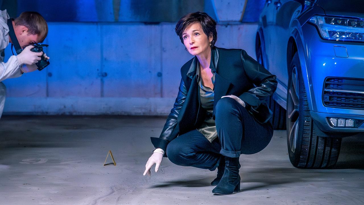 Katharina Stemberger zeigt am Tatort in einer der Tiefgarage auf etwas am Boden