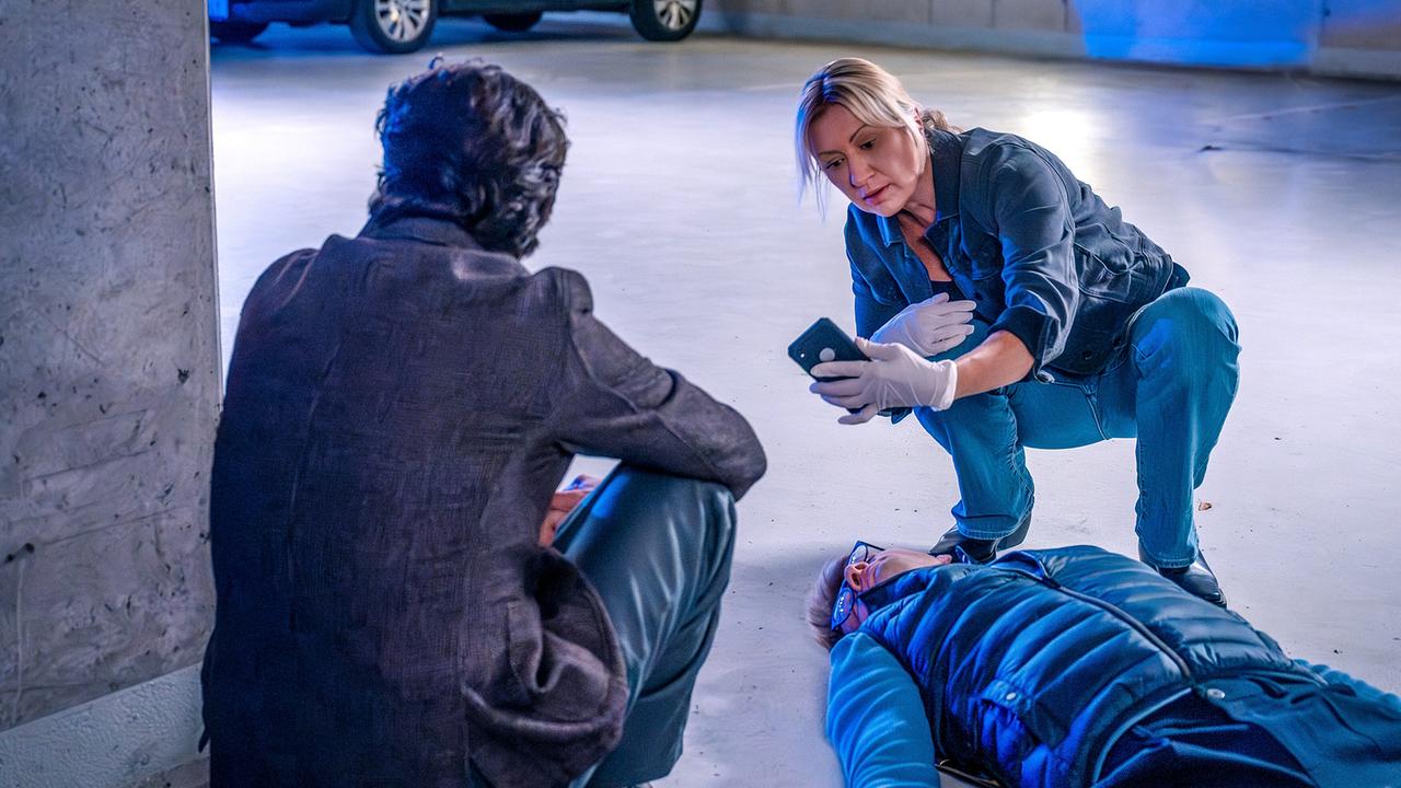 Angelika Niedetzky fotografiert in einer Tiefgarage die Leiche von Max Häusle mit ihrem Smartphone, daneben Alexander Pschill 