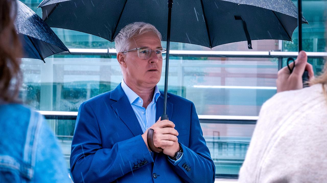 Arthur Klemt unter einem Regenschirm vor einer Glasfassade