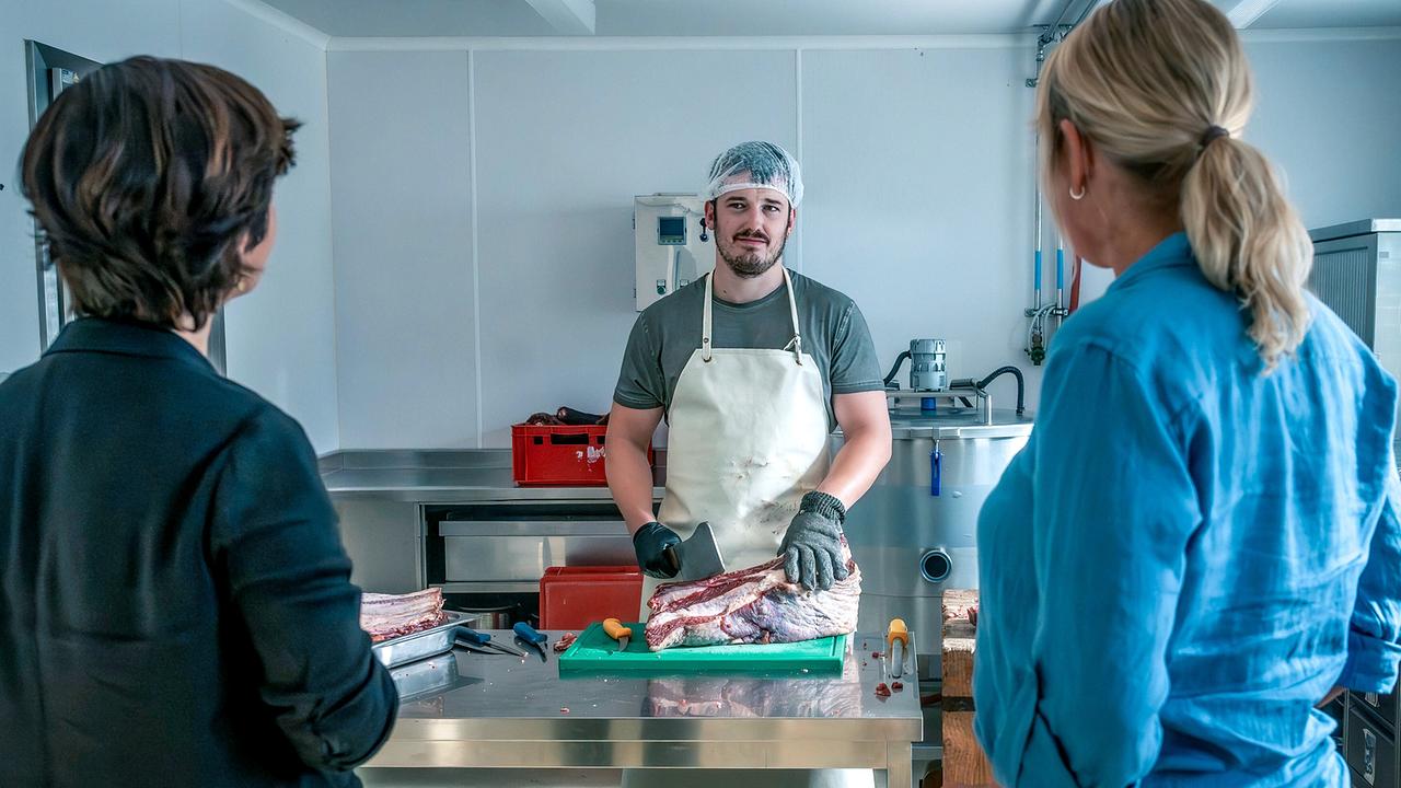 Katharina Stemberger und Angelika Niedetzky beobachten einen Metzger bei der Fleischverarbeitung.