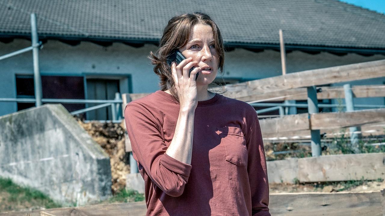 Anna Rieser am Handy vor einem Bauernhofgebäude