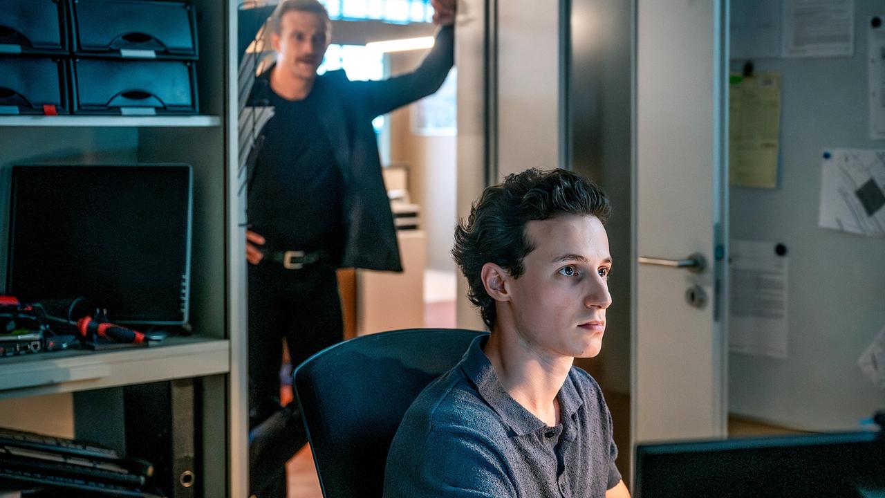 Szene in einem Büro mit zwei Männern, Damyan Andreev sitzt am Computer und Michael Steinocher lehnt an einer Tür.