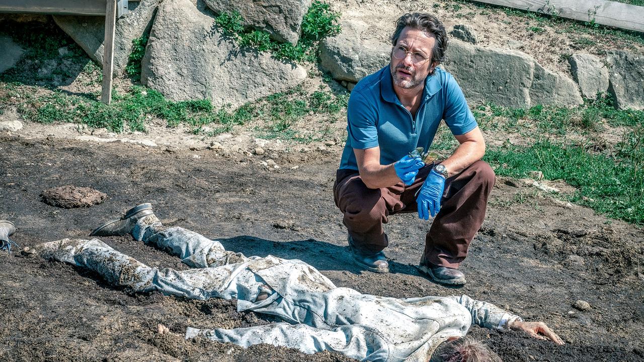 Alexander Pschill kniet neben einer am Boden liegenden, verschmutzten Leiche.