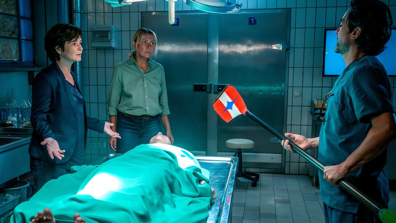 Katharina Stemberger, Angelika Niedetzky und Alexander Pschill, der ein Ruderblatt hält, stehen im Obduktionsraum um eine zugedeckte Leiche