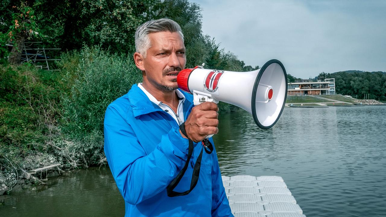Faris Rahoma steht mit einem Lautsprecher in der Hand am Flussufer