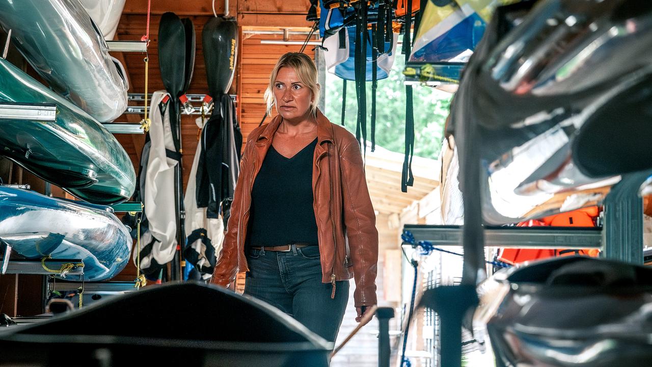 Angelika Niedetzky in Lederjacke steht in einem Bootshaus zwischen aufgestapelten Kanus und Ausrüstung.