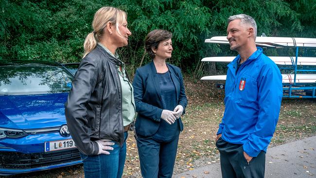 © ORF/Gebhardt Productions/Stefanie Leo Angelika Niedetzky und Katharina Stemberger unterhalten sich vor einem Auto im Freien mit Faris Rahoma, im Hintergrund gestapelte Ruderboote