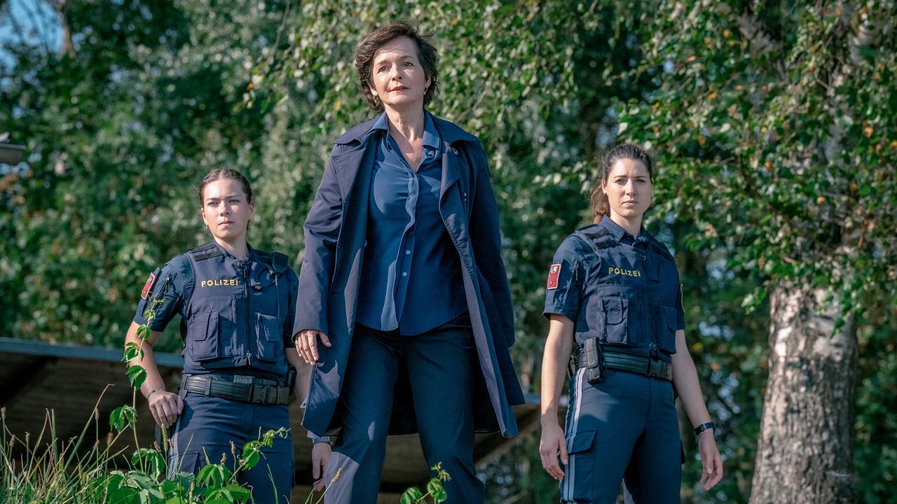 Katharina Stemberger mit zwei Polizistinnen blicken im Freien auf etwas