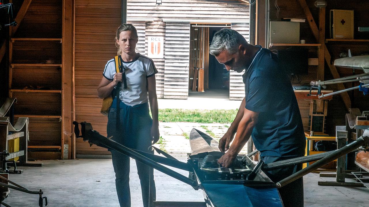 Viktoria Hauer blickt in einem Bootshaus auf Faris Rahoma, der an einem Ruderboot arbeitet.