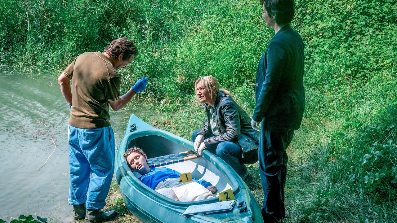 Alexander Pschill, Angelika Niedetzky und Katharina Stemberger untersuchen eine Leiche in einem Kajak am Ufer