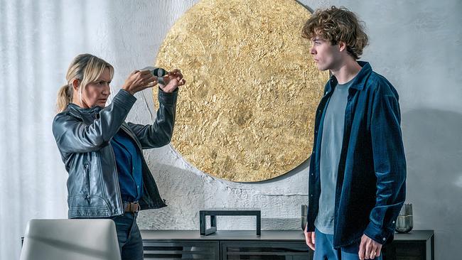 © ORF/Gebhardt Productions/Stefanie Leo Angelika Niedetzky begutachtet in einem Büro vor einem goldfarbenen, kreisrunden Bild ein silberfarbenes, technisches Gerät in ihren Händen, Lino Gaier sieht ihr zu