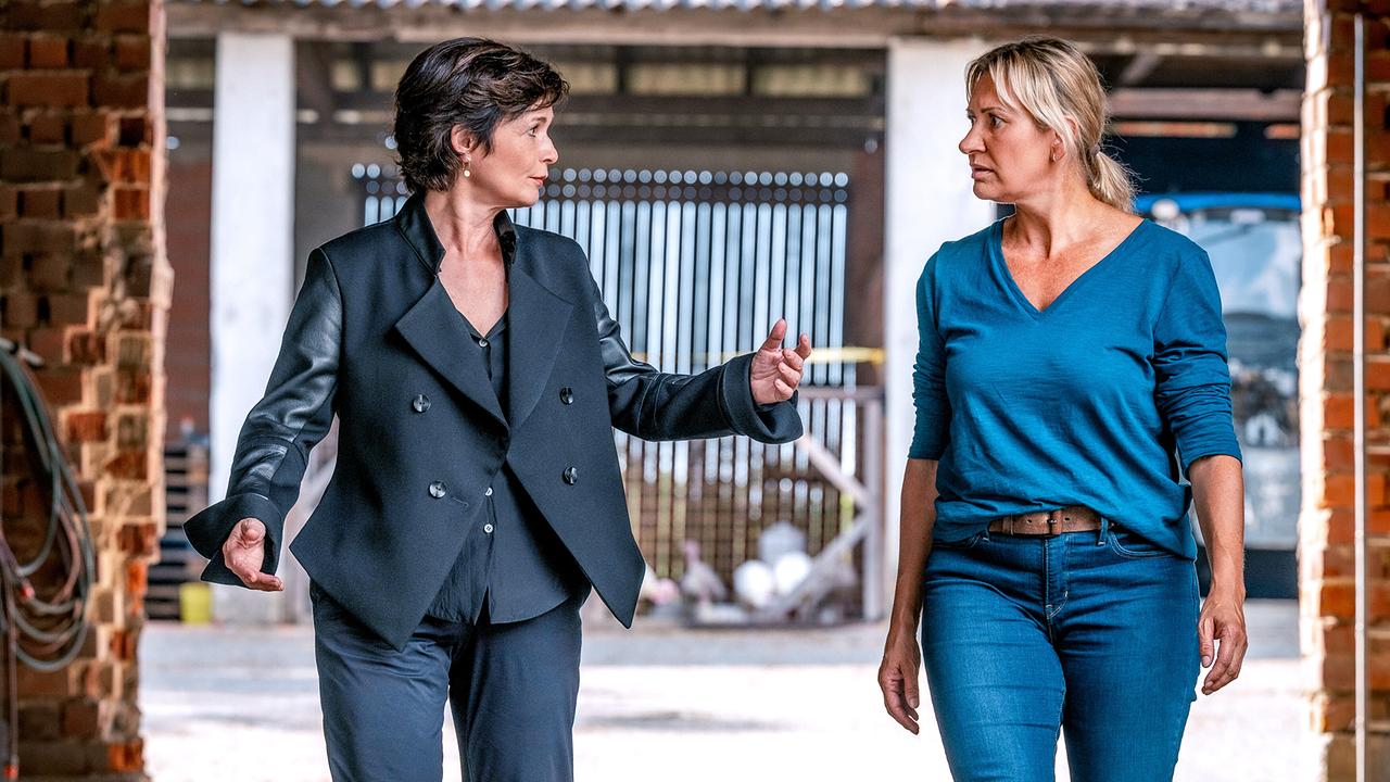 Katharina Stemberger und Angelika Niedetzky gehen nebeneinander durch einen offenen Bereich mit Backsteinmauern.