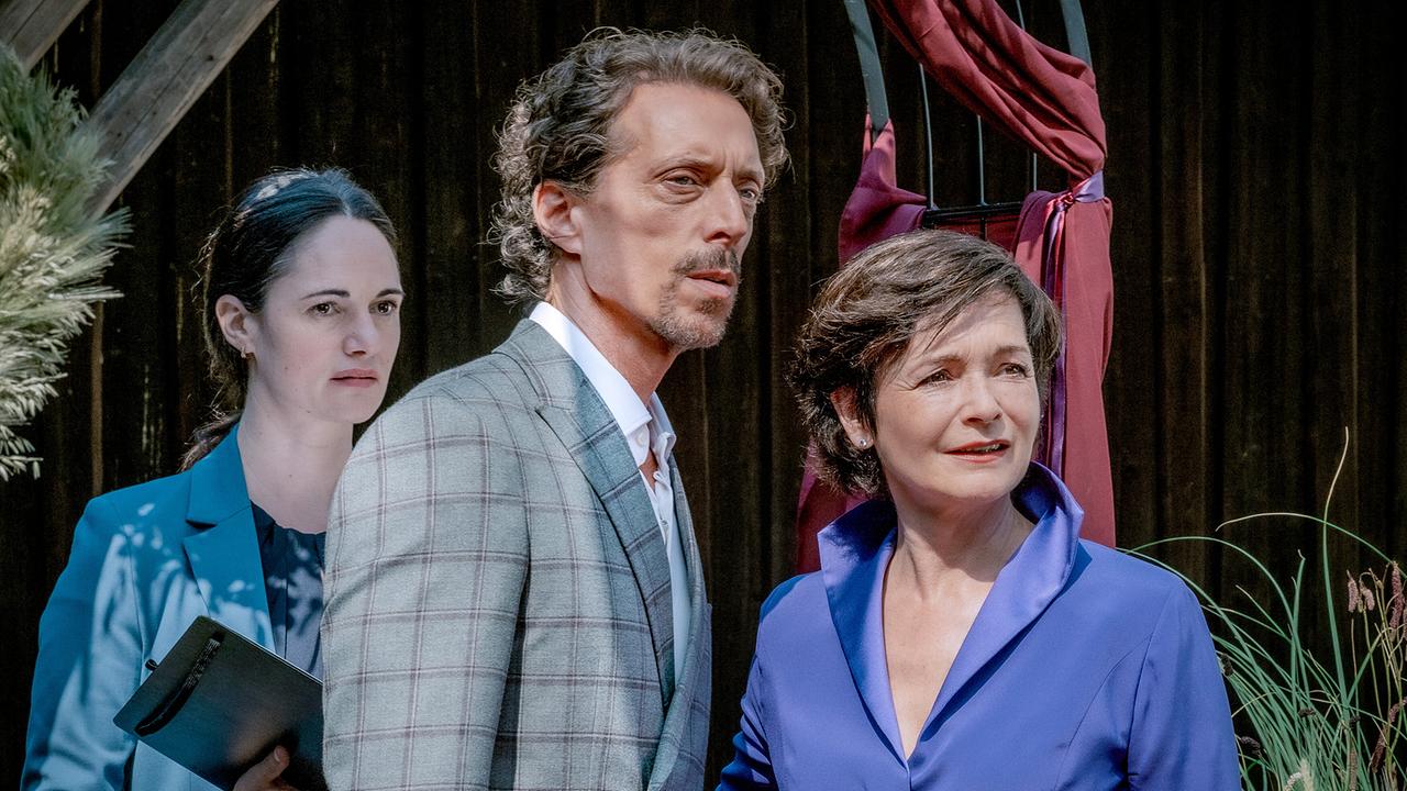Stefanie Altenhofer als Standesbeamtin, Michael Pink und Katharina Stemberger unter einem Traubogen schauen gespannt in eine Richtung.