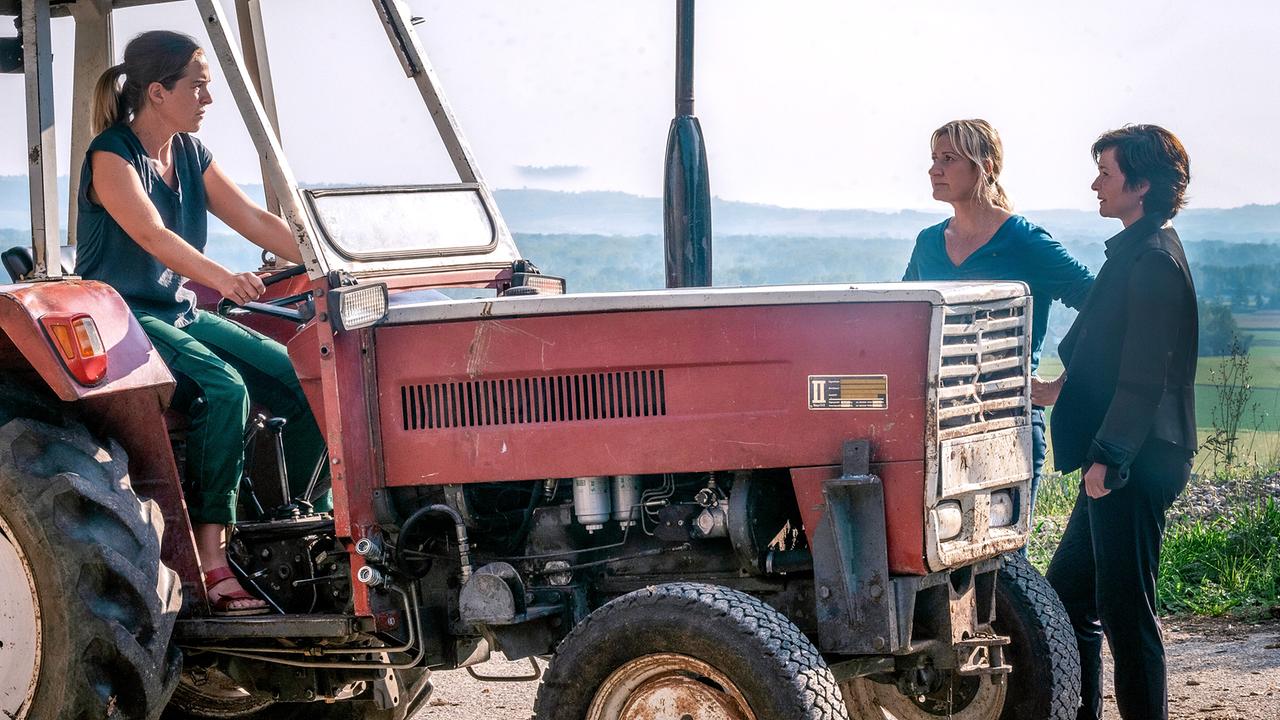 Nikola Jaritz-Rudle sitzt auf einem roten Traktor, während Angelika Niedetzky und Katharina Stemberger danebenstehen und sich mit ihr unterhalten.