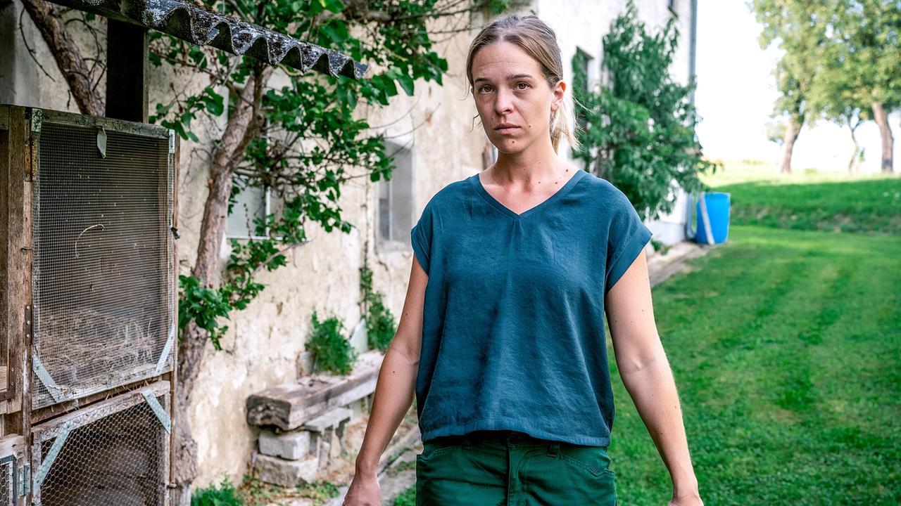 Nikola Jaritz-Rudle schiebt eine Schubkarre im Garten neben einem alten Gebäude und schaut ernst.