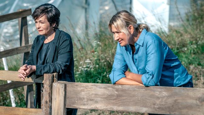 © ORF/Gebhardt Productions/Stefanie Leo Katharina Stemberger und Angelika Niedetzky lehnen an einem Holzzaun im Freien vor einem Gewächshaus.