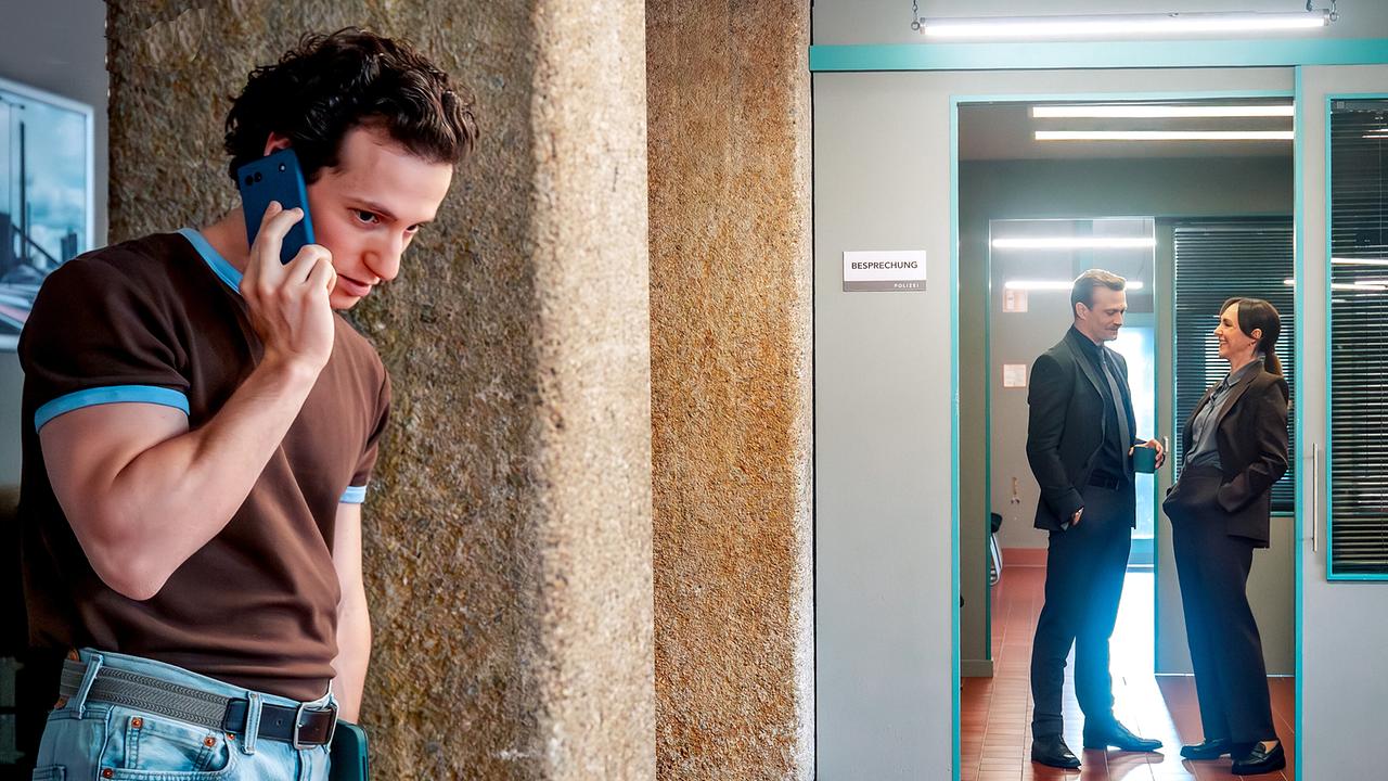 © ORF/Gebhardt Productions/Stefanie Leo Aleks Malenov telefoniert am Gang im Kommissariat, während sich die zwei Kolleg:innen Stefan Pichlwanger und Patrizia Specht im Hintergrund unterhalten.