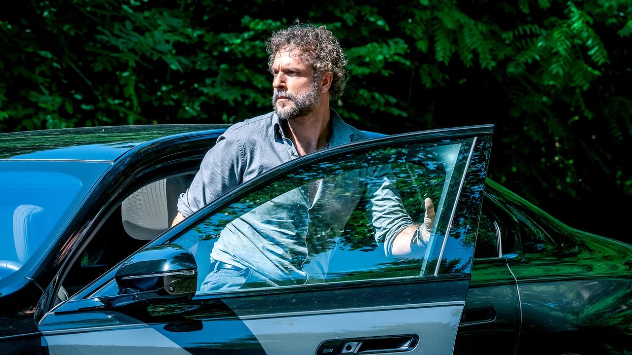 Hannibal Warga, ein bärtiger Mann, steigt neben einem dichten Grün bei Sonnenschein aus einem dunklen Auto aus.
