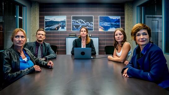 Biggi Obergschwendter, Stefan Pichlwanger, Emilia Ertl und Joe Haizinger sitzen an einem Besprechungstisch mit Sarah Lorenzoni vor einem Laptop am Kopf des Tisches. Sie alle schauen auf etwas vorne außerhalb des Bildes.