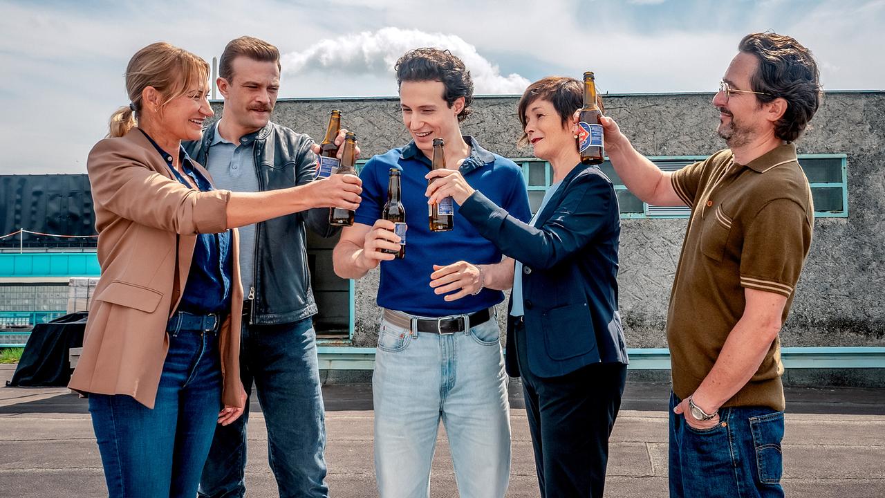 Biggi Obergschwendter, Stefan Pichlwanger, Aleks Malenov, Joe Haizinger und Dr. Richie Vitek stoßen auf einem Dach mit Bierflaschen an.
