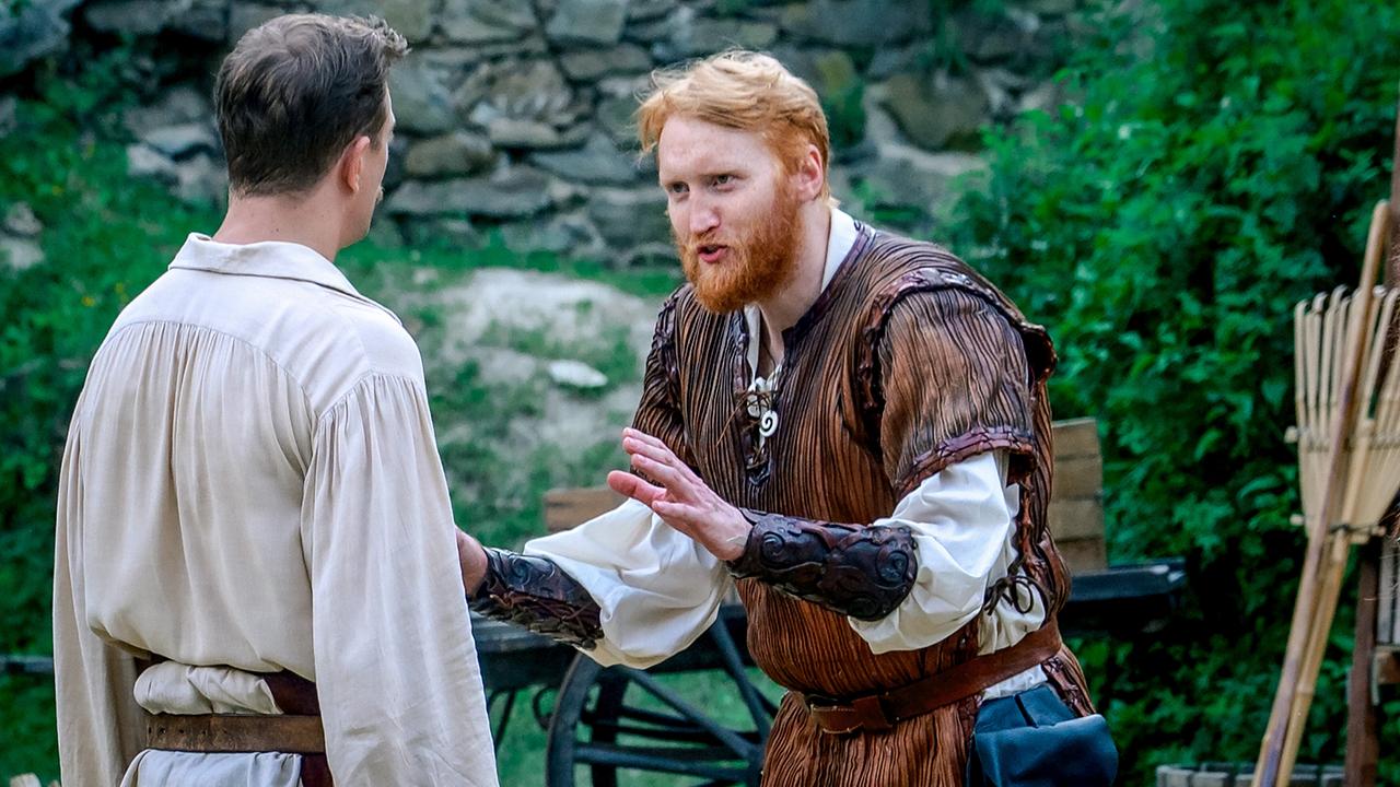 Der rothaariger Olli Moors in mittelalterlicher Kleidung spricht eindringlich mit Stefan Pichlwanger in hellem Gewand vor ihm.