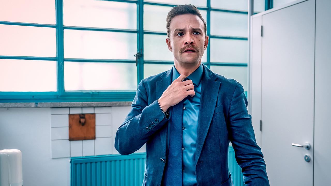 Stefan Pichlwanger im Anzug richtet in einem hellen öffentlichen WC vor dem Spiegel seine Krawatte.