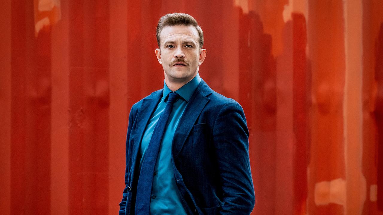 Stefan Pichlwanger  im Anzug steht ernst vor einer rötlichen Wand.
