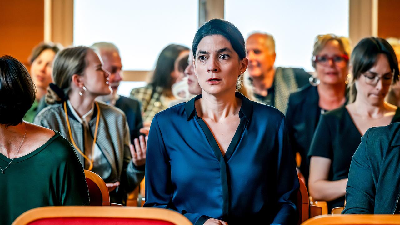 Anja Schlott im blauen Blazer blickt besorgt zwischen den übrigen Zuhörenden im Gerichtssaal nach vorne.