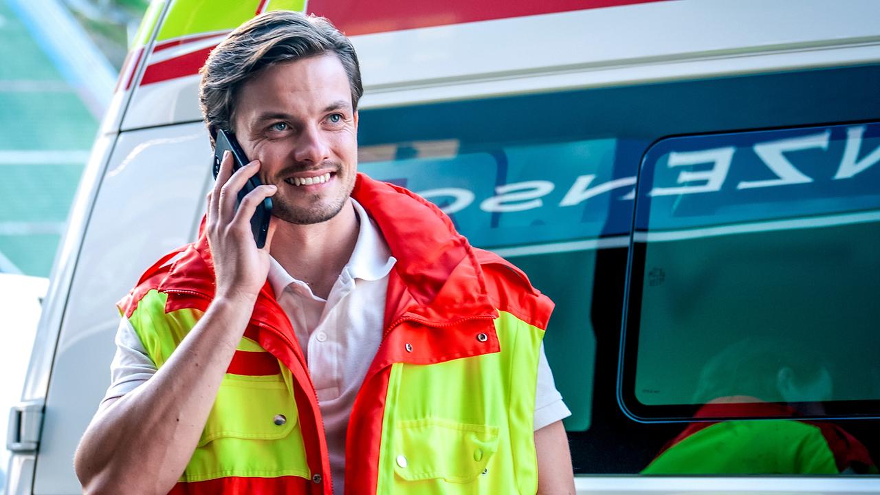 Der lächelnde Sanitäter Jonathan Migler telefoniert vor einem Rettungswagen. 