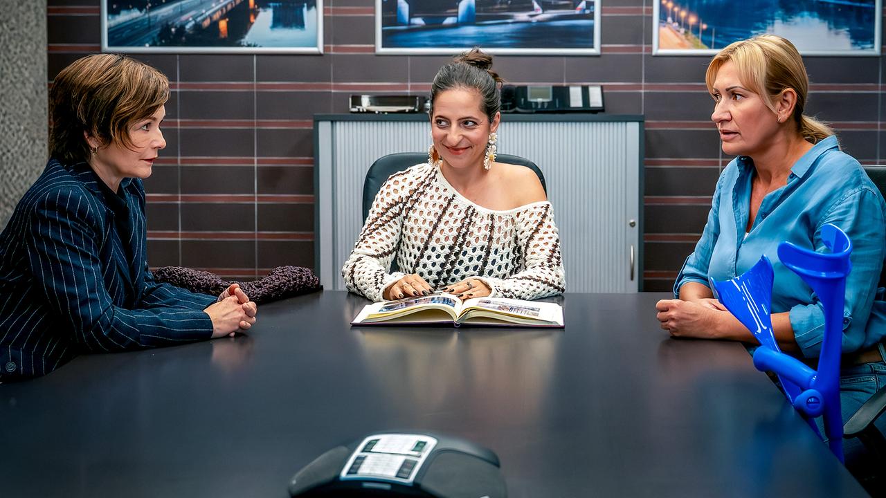 Joe und Biggi sitzen mit Jaqueline Pfaffenebner an einem Besprechungstisch, vor ihnen liegt ein offenes Fotoalbum.