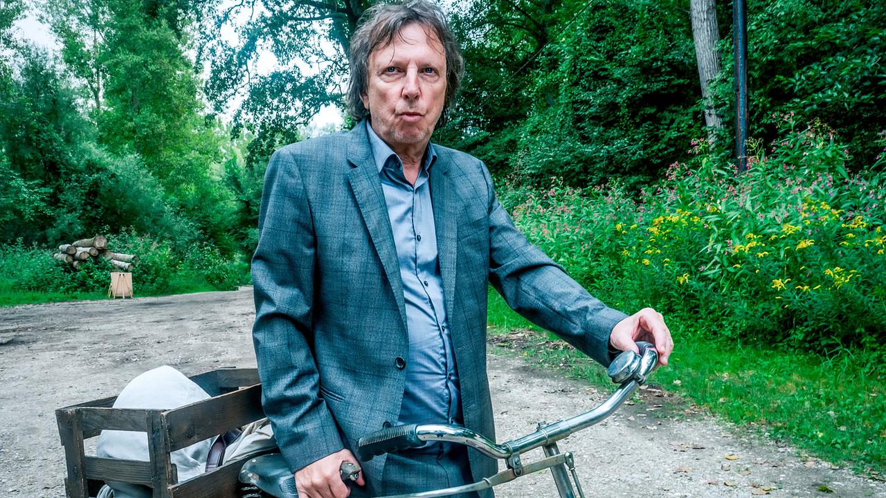 Joachim "Habi" Haberstetter  im Anzug steht mit einem Lastenfahrrad auf einem Weg im Grünen.