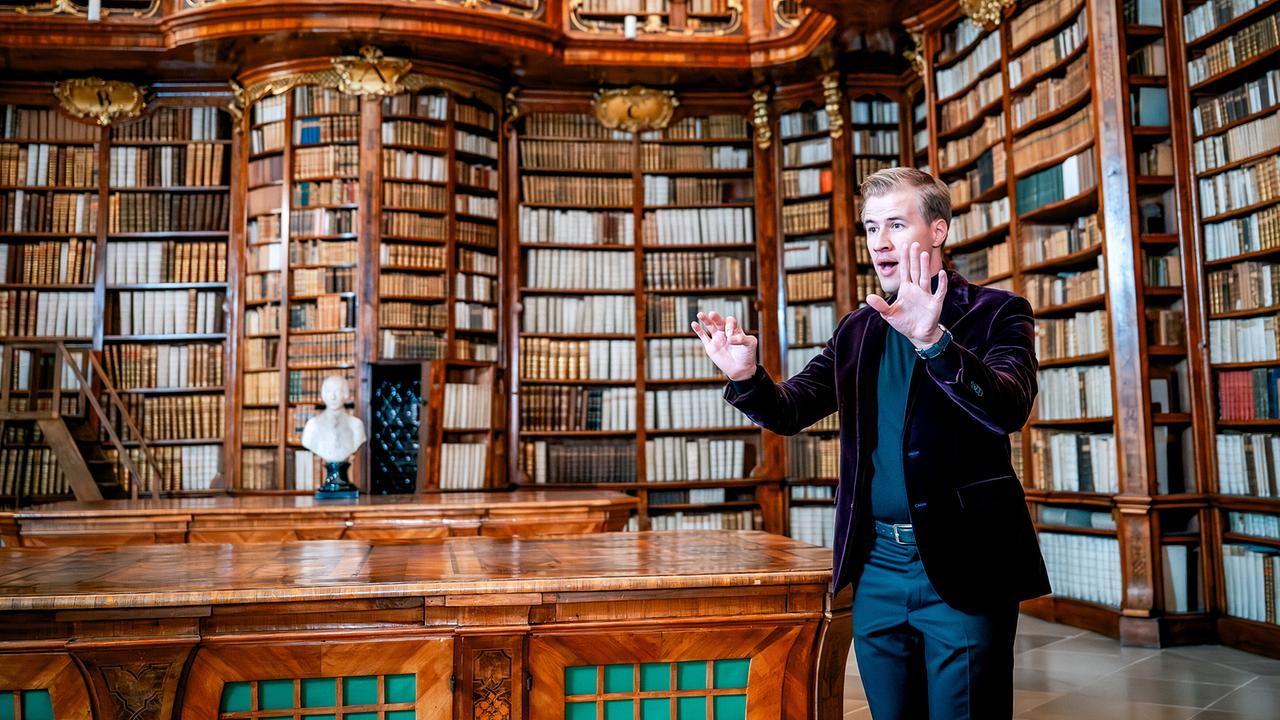 Ein Mann gestikuliert mit abwehrenden Händen in der prunkvollen historischen Bibliothek von St. Florian.