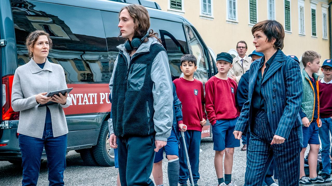 Enno Tomberg und Joe Haizinger gehen im Freien an Isolde Überbacher und mehreren Buben vor einem Transporter vorbei.