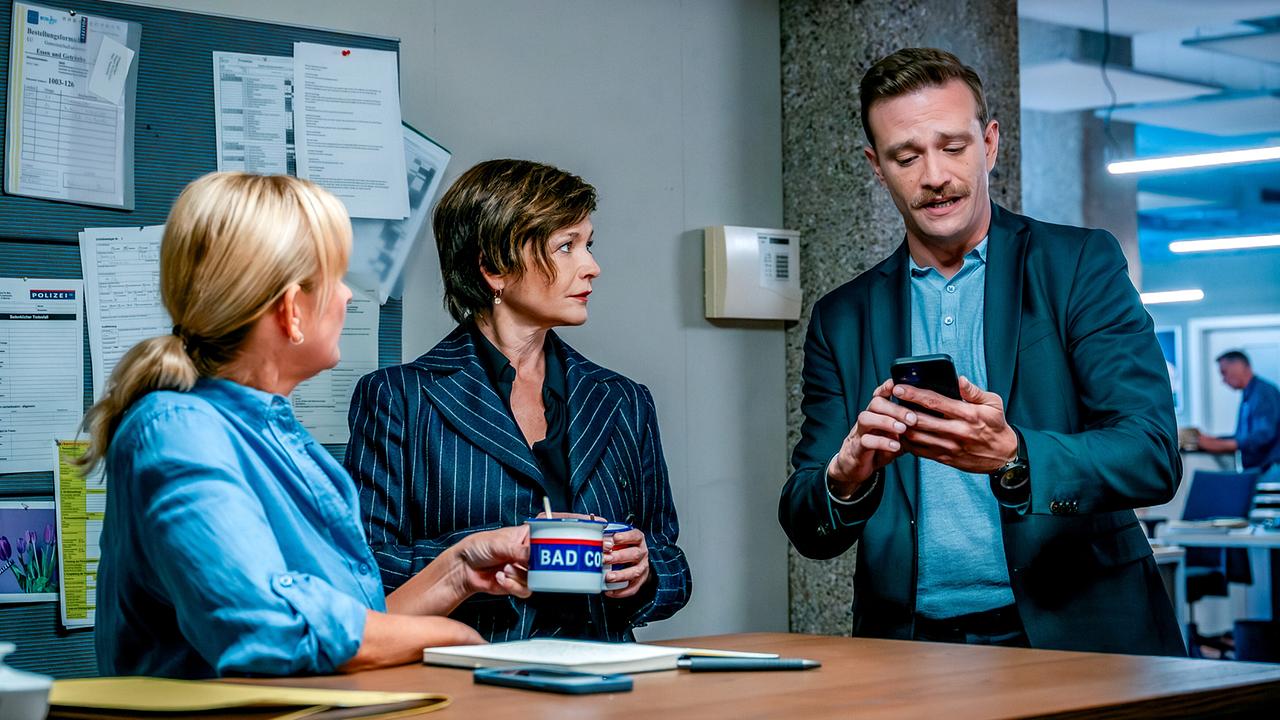 In einer Polizeidienststelle zeigt Stefan Pichlwanger Biggi und Joe etwas auf seinem Smartphone.
