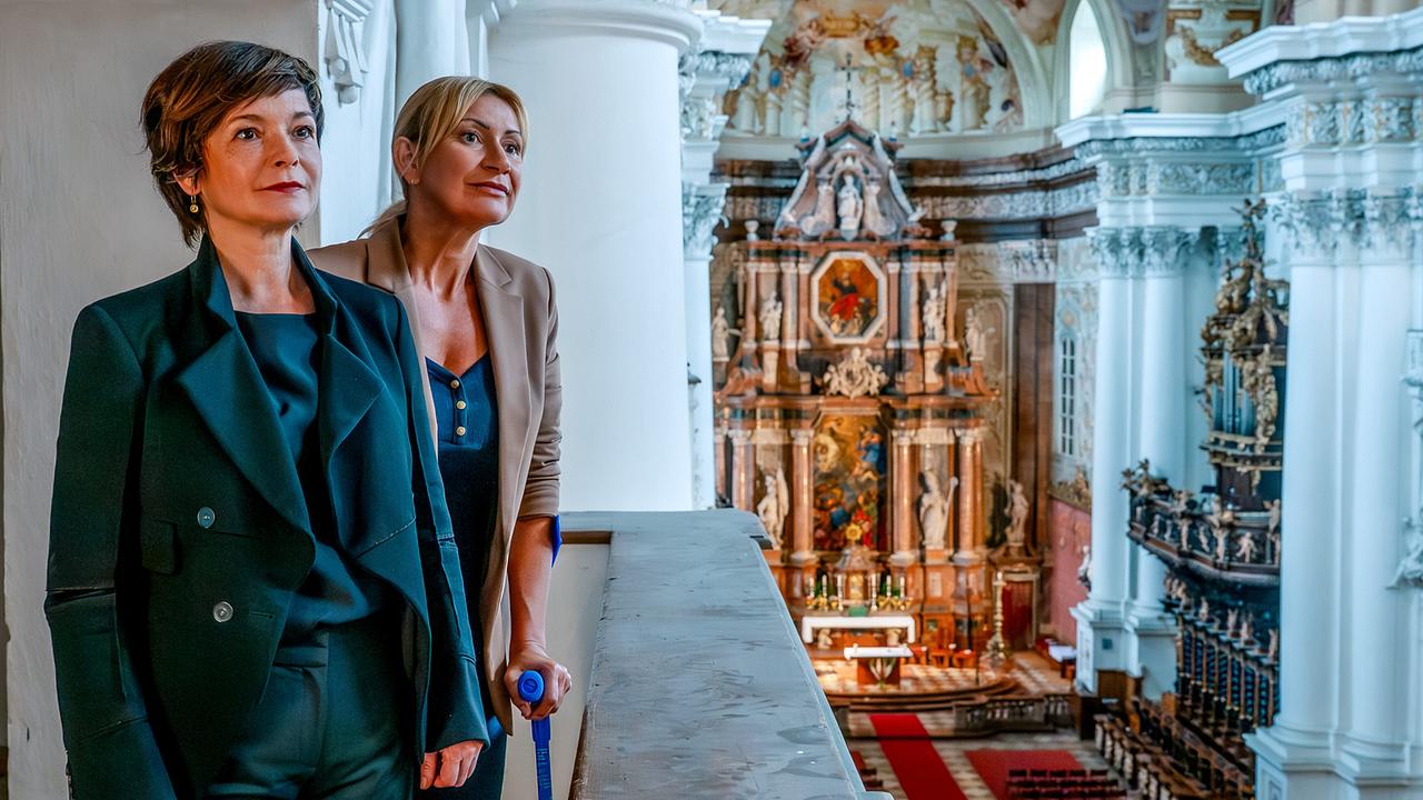 Joe und Biggi stehen auf einer Empore und blicken in das prunkvolle Innere der barocken Stiftskirche St. Florian.