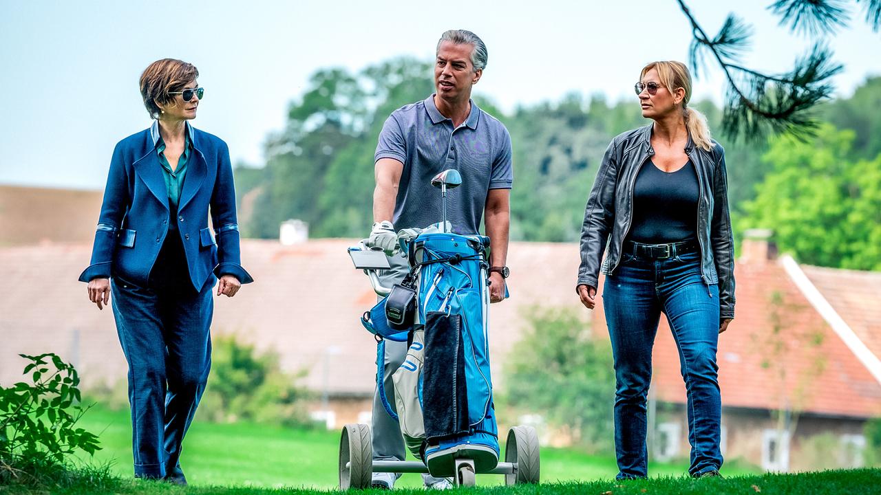 Joe Haizinger und (Biggi Obergschwendter begleiten Kurt Schweigauer mit Golftasche über einen Golfplatz.