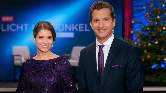 Kristina Inhof und Oliver Polzer in festlicher Kleidung stehen in einem Studio vor einem beleuchteten Hintergrund mit Weihnachtsbaum und ORF‑"Licht ins Dunkel"-Logo.