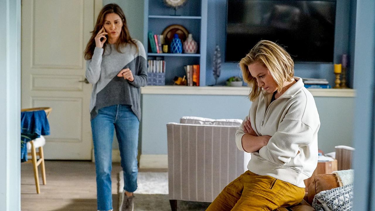 © ORF/Disney/ABC/Kelsey McNeal Zwei junge Frauen in einem blauen Wohnzimmer, eine telefoniert am Handy und geht durch den Raum, die andere sitzt mit verschränkten Armen auf der Sofalehne und blickt vor sich auf den Boden