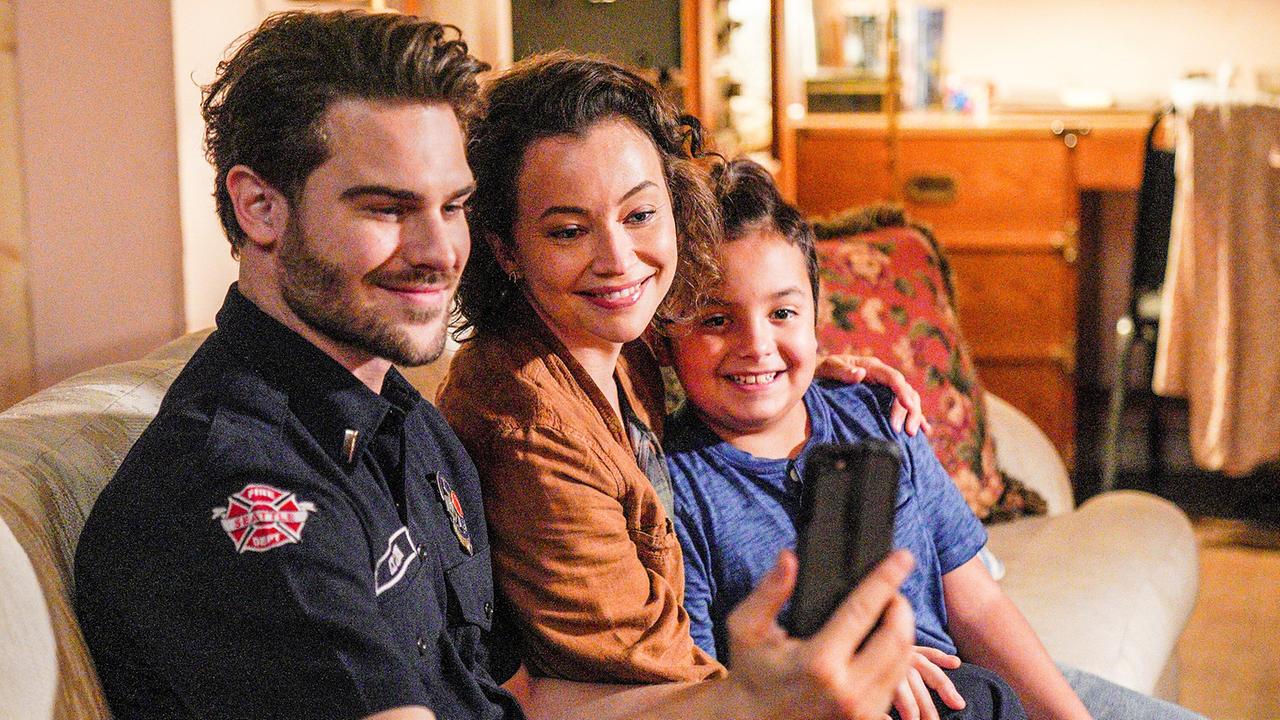© ORF/Disney/ABC/Christopher Willard Ein Mann in kurzärmeligem, schwarzen Hemd mit Feuerwehr-Abzeichen sitzt im Wohnzimmer auf einer Couch neben einer Frau und einem Kind, mit seinem Handy macht ein Selfie - alle lächeln freundlich