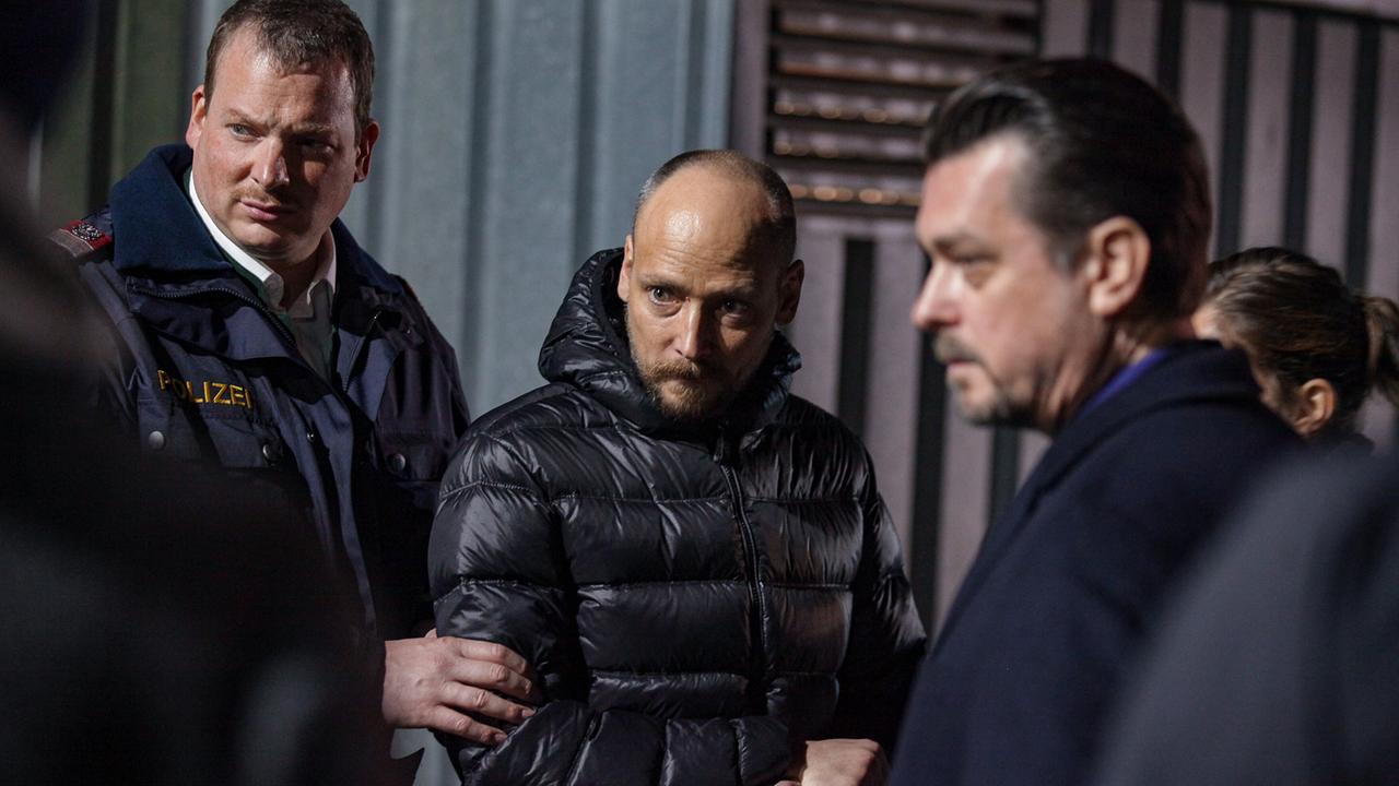 Ferdinand Franz in Polizeiuniform hält Zlatko am Arm in dunkler Umgebung, um die beiden herum stehen Sascha Bergmann und Sandra Mohr.