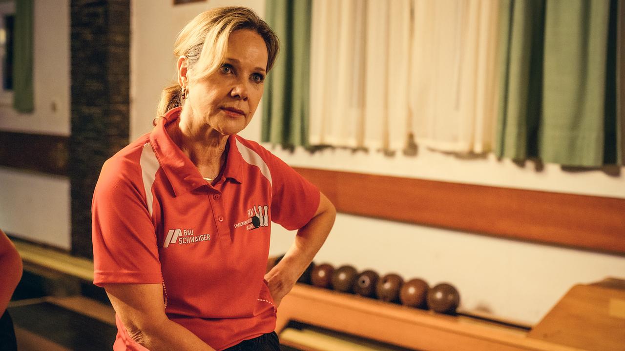 Ingrid Trieber  in Sportkleidung sitzt am Rand einer Kegelbahn und schaut zu jemandem.