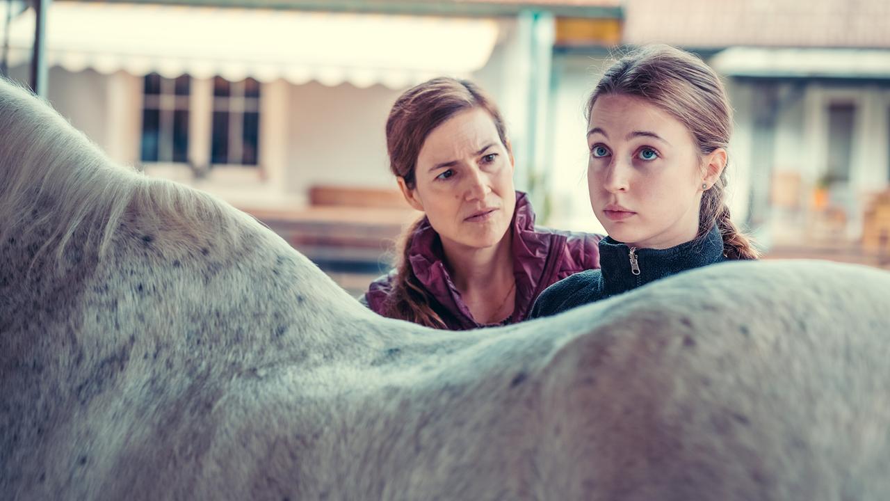 Miriam und Rita Messner stehen neben einem weißen Pferd und schauen ernst.