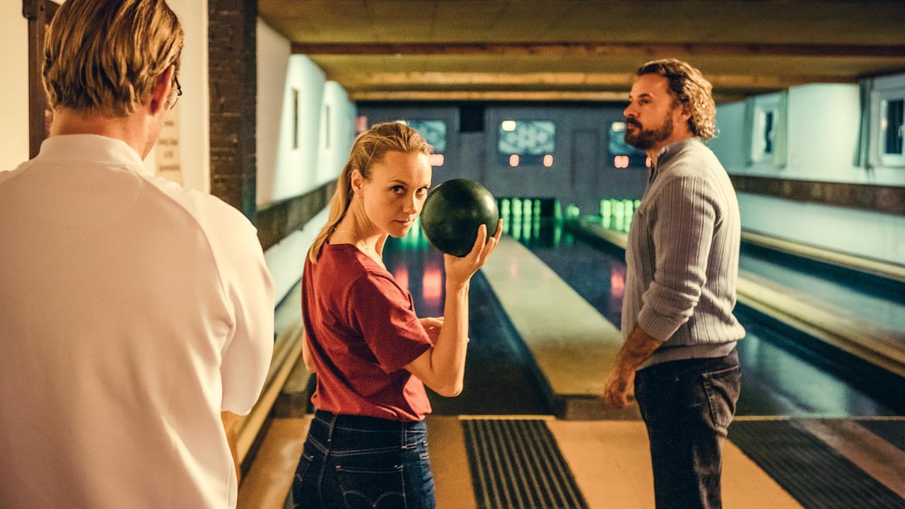 Anni Sulmtaler hält auf einer Kegelbahn eine Kugel bereit, während zwei Männer ihr zuschauen.