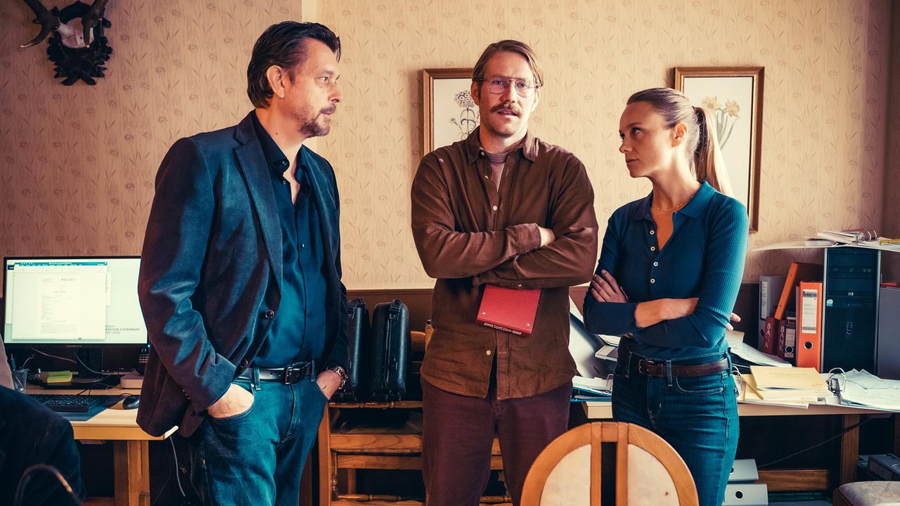 Sascha Bergmann, Bernd Kofler und Anni Sulmtaler stehen in einem Büro voller Akten und Computer und führen ein Gespräch.