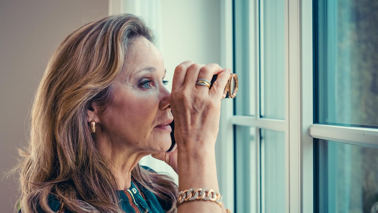 Ingrid Trieber schaut durch ein Fernglas aus einem hellen Fenster.